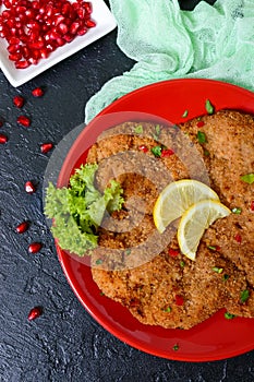 Large Viennese schnitzel on a red plate with lemon on a black background. Meat dish.