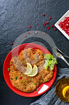 Large Viennese schnitzel on a red plate with lemon on a black background. Meat dish.