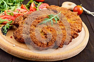 A large Viennese schnitzel and tomato salad on a cutting board on a dark wooden background.