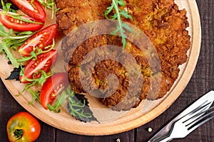 A large Viennese schnitzel and tomato salad on a cutting board on a dark wooden background.