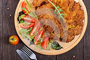 A large Viennese schnitzel and tomato salad on a cutting board on a dark wooden background.