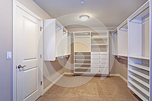 Large walk-in closet with white shelves, drawers photo