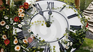 Large wall clock on the field in blooming flowers, showing the time 11:55, 12:00. time management concept, daylight