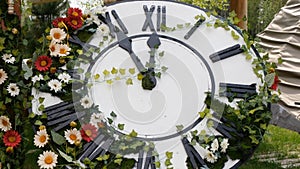 Large wall clock on the field in blooming flowers, showing the time 11:55, 12:00. time management concept, daylight