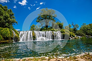 a large waterfall is surrounded by greenery and trees in a blue sky