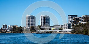 Large waterfront apartment condominiums in suburban community on harbour with tree lined walkway, blue sky in background