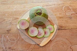 Large watermelon radish and radish slices on a bamboo cutting board, vintage wood table