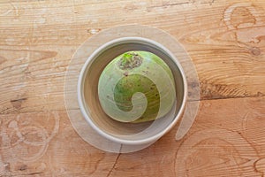 Large watermelon radish in a small white bowl, overhead view, old wood background