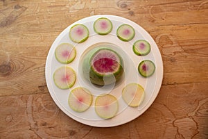 Large watermelon radish in a white bowl surrounded by radish slices on old wood background