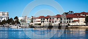 Large waterside houses, apartment condominiums in suburban community on riverfront with boat moored at wharf, blue sky in backgrou