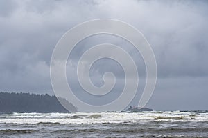Large waves crash to shore at Deep Bay beach on a dreary and stormy day on Vancouver Island. Boyle Point lighthouse off