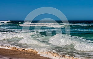 Large waves rolling in to the beach from a turqoise sea under a blue sky photo