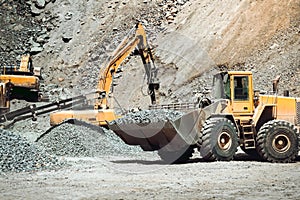 Large wheel loader on construction site transporting and loading gravel into dumper trucks