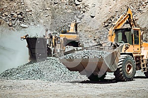 Large wheel loader on construction site transporting and loading gravel into dumper trucks