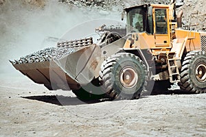 Large wheel loader on quarry site transporting and loading gravel into dumper trucks