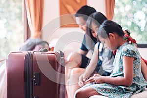 Large wheeled suitcase standing on the floor in the hotel room with happy asian family sitting on the bed in background