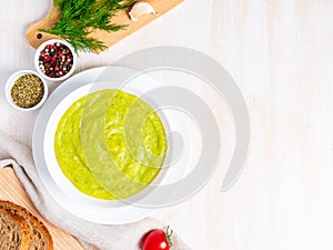 Large white bowl with vegetable green cream soup of broccoli, zucchini, green peas on white background, top view, copy space