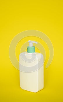 Large white cosmetic plastic bottle with pump dispenser pump and green cap on yellow background. Liquid container for