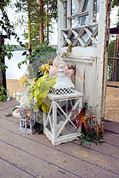 Large white decorative candle lantern and small candle lantern stand on terrace with flowers and autumn leaves. Wedding decor.