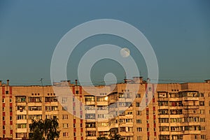 Large white full moon on clear blue over an urban city high building