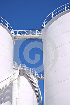 Large white industrial tanks with metal stairs for petrol and oil with blue clear sky background