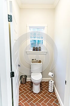 Large white renovated master bathroom toilet area with red brick floors