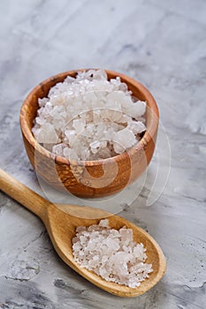 Large white sea salt in a natural wooden bowl on light background, top view, close-up, selective focus