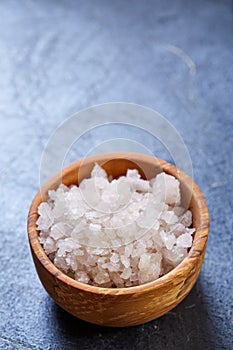 Large white sea salt in a natural wooden bowl on dark background, top view, close-up, selective focus