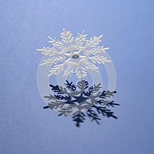 A large white snowflake and its shadow on a blue background. Minimal winter concept