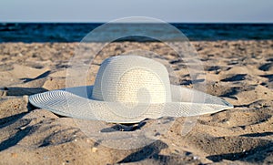 Large white straw hat on the soft sand against the background of the sea. Beach accessories.