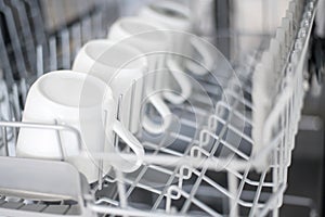 Large white tea mugs are stacked in the dishwasher