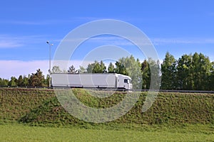 Large white truck moves on road on hill in green grass