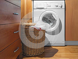 Large Wicker Laundry Basket, Open Lid Near the Washing Machine with Laundry. House Interior Laundry Room. Wood Interior Design