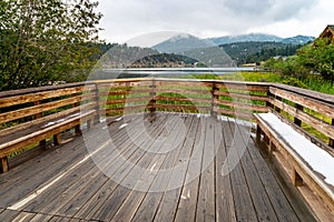 A large wood patio by a lake with mountains in the background