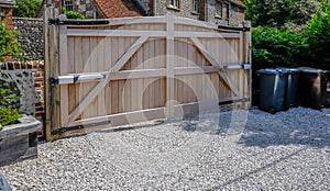 Large wooden entry electric gates with stone driveway