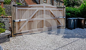 Large wooden entry electric gates with stone driveway photo