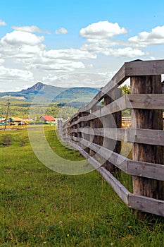 A large wooden fence on a private plot in the village of Shigaevo in the Southern Urals against the backdrop of mountains and Arvy
