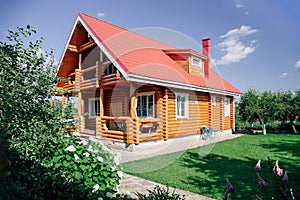 Large wooden newly built country house with red tile roof, lawn area on right and cherry trees orchard behind house and