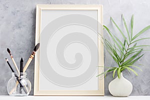 Large wooden Photo frame mock up with green palm leaves in vase and brushes in glass on shelf. Scandinavian style