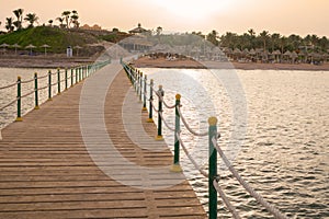 A large wooden pier is on the sandy beach of the resort. Beautiful view of the tropical coast with a long pantone. Landscape of