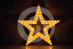 Large wooden star with a large amount of lights in front of dark concrete background.