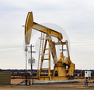 Large Yellow 912 Pump Jack on oil or gas well with surrounding equipment against an overcast sky