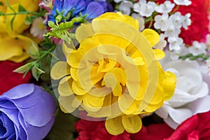 Large yellow artificial flower surrounded by smaller flowers close view