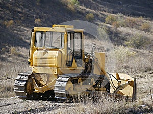 A large yellow bulldozer flattens a mountain dirt road in clouds of dust on a Sunny autumn day