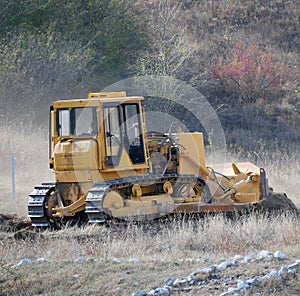 A large yellow bulldozer flattens a mountain dirt road in clouds of dust on a Sunny autumn day