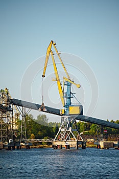 Large yellow crane standing on a dock by a river, with a bridge in the background