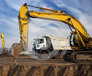 large yellow crawler excavator and a gray dump truck stand at a construction site