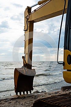 Large yellow excavator works on seaside. Construction on the coast