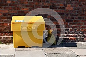 Large yellow grit salt container on pavement sidewalk