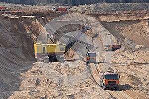 Largest mining excavator with electric shovel loading sand into dump truck in opencast. Orange mining trucks transports sand